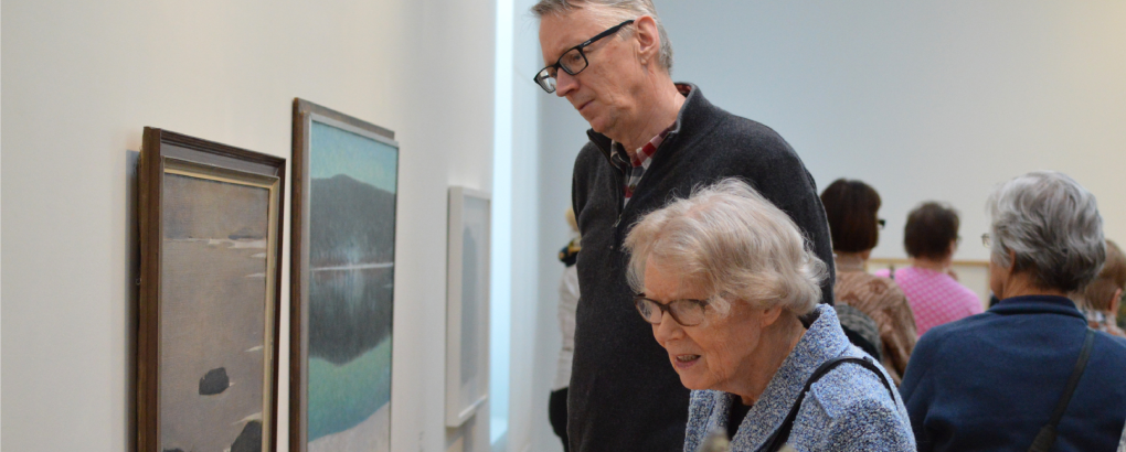 Harmaantuneet mies ja nainen katselevat maalauksia galleriatilassa.